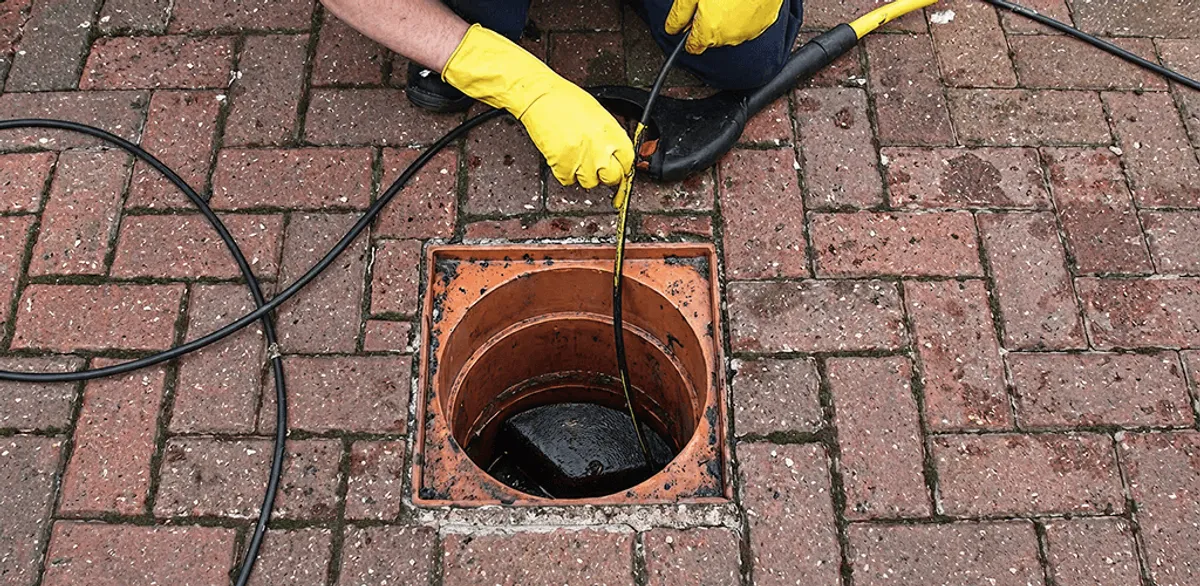 Drain cleaning technician using a drain snake to clear a clogged drain in San Diego, CA